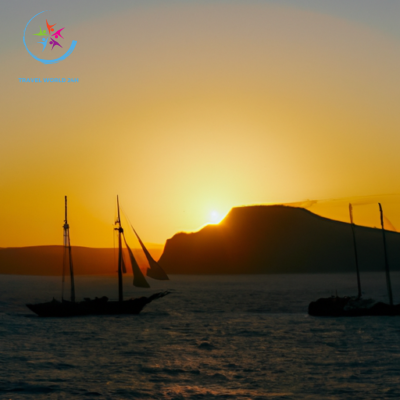 the enchantment of a Greek island sunset cruise: A vibrant orange sun dips below the azure horizon, casting a warm glow on the tranquil Aegean Sea